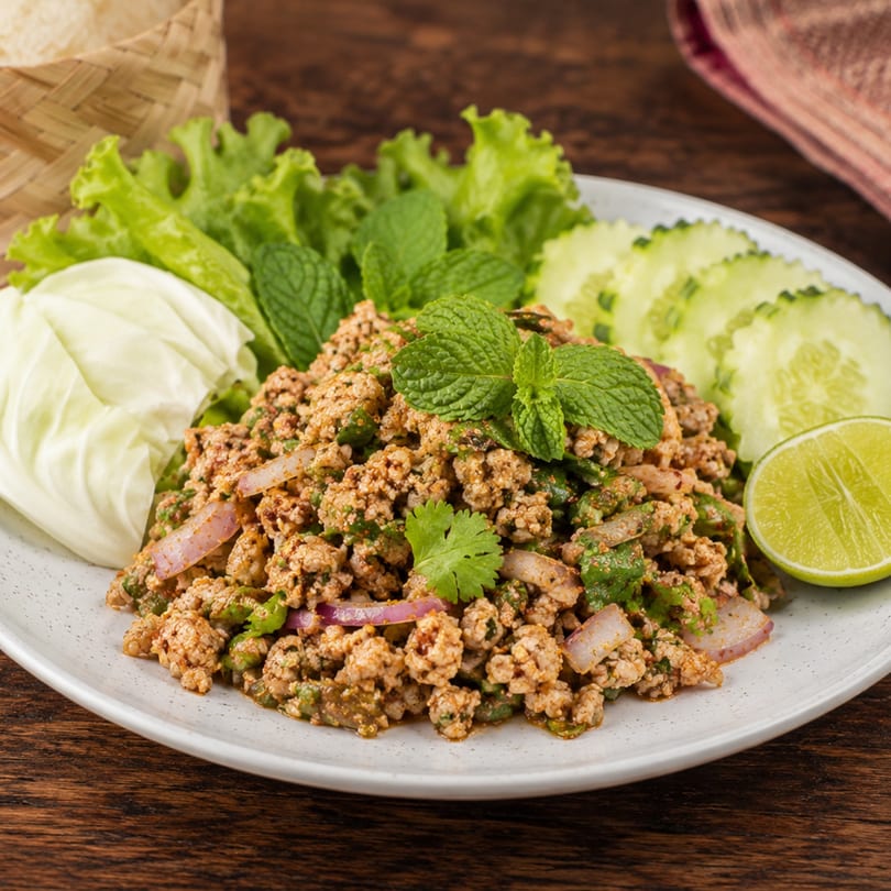 Spicy minced meat salad (Larb) with fresh mint, cilantro, red onion, lime, and lettuce.